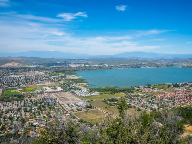 Aerial view of a city surrounding a large lake with mountains in the background under a blue sky.
