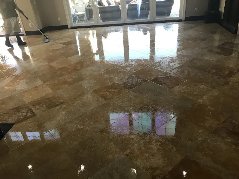Person cleaning or polishing a shiny tiled floor in a room with large windows.