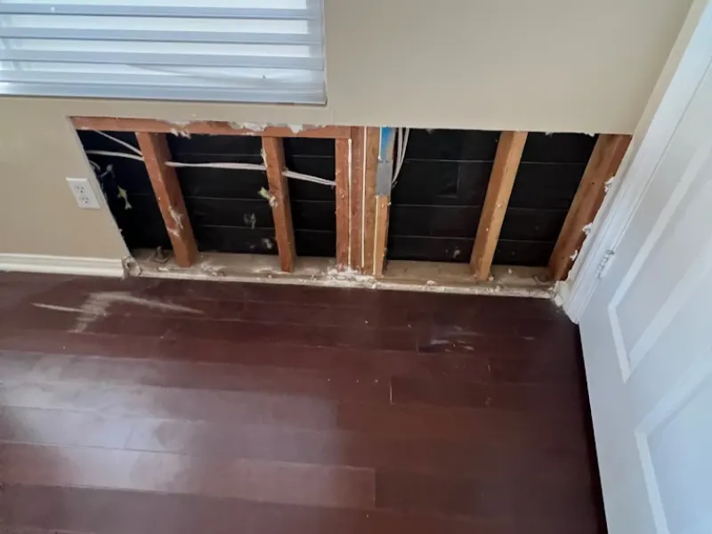 Section of wall drywall removed exposing wooden studs and wiring behind it.